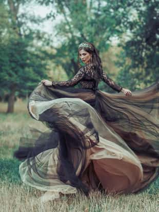 Glamorous fashion woman in long luxurious black dress with beige color Dancing spinning. Backdrop autumn nature. Gothic fantasy beauty Attractive sexy Dark Queen. Train skirt flutters waving in motion