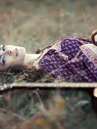 Beautiful hippie girl with guitar lying on the grass
