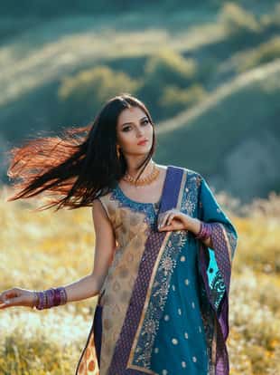 Beautiful girl with dark hair Oriental appearance, dancing among the fields of flowers at sunset. The image on the background of picturesque hills. Fashionable tinted. Creative color.