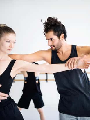Male coach adjusting posture of female dancer at studio. Young ballet dancers are practicing at dance studio. They are rehearsing against wall.