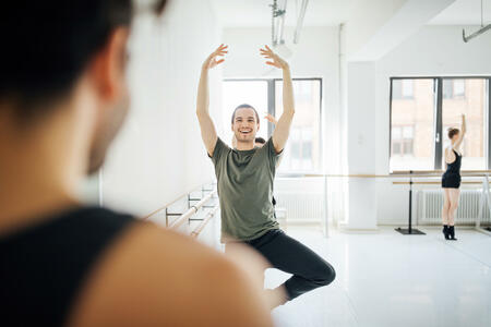 Smiling male dancer practicing ballet with arms raised. Young performer rehearsing by barre at dance studio. They are practicing at ballet studio.
