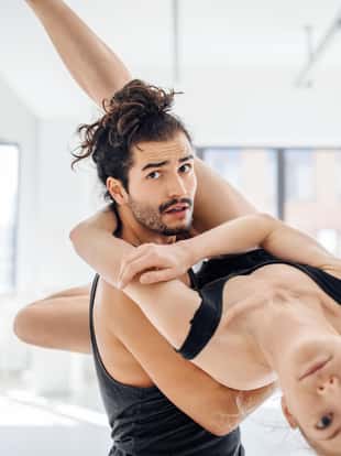 Multi-ethnic man and woman dancers rehearsing ballet. Young male picking female while dancing at studio. Flexible performers are in sportswear.