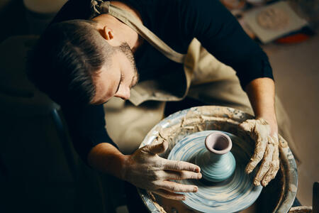 Potter modeling ceramic pot from clay on a potter's wheel. Workshop, art concept