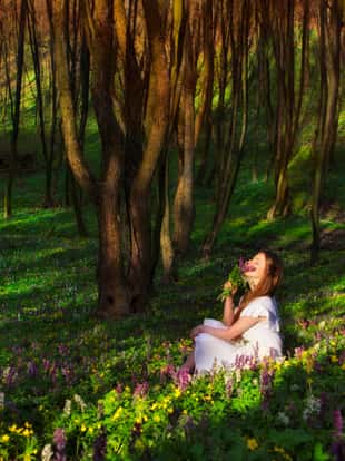A woman is sitting on a meadow with flowers and enjoying the beauty of nature