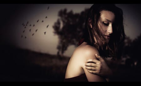 Conceptual shot of a young woman in red dress in a gloomy romantic landscape with a flock of red birds in the background