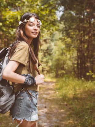 Portrait of young woman hiking in forest. Beautiful hipster is carrying backpack. Adventurous female is enjoying her summer vacation.