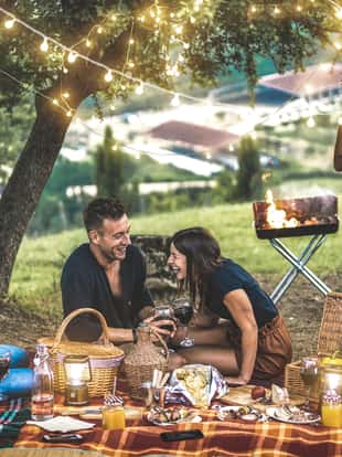 Happy friends having fun at vineyard after sunset - Young people millennial camping at open air picnic under bulb lights - Youth friendship concept with young people drinking wine at barbecue party