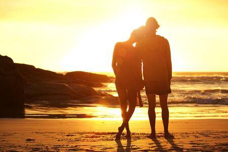 Full length portrait of a loving couple standing by the beach looking at sunset