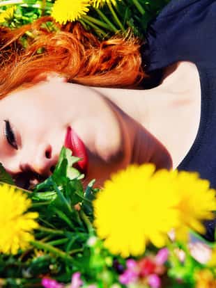 photo of girl with red hair lying on the field of dandelions