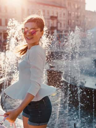 Happy young woman tourist having fun in the city by fountain at sunset. Summer holidays. Travelling around the world