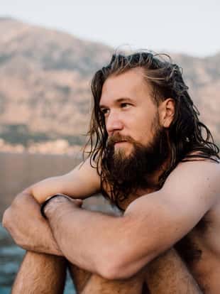 Stock photo of a young bearded man with long hair sitting near the sea
