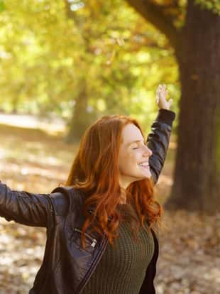 Young cheerful red-haired woman enjoying sunny autumn day in park