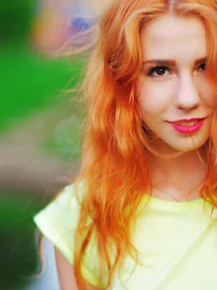 A wonderful portrait of a beautiful young woman with red hair and bright makeup outdoors in the summer.