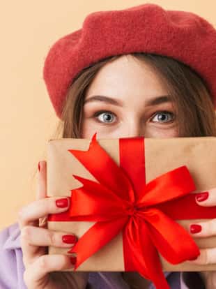 Image of brunette woman 20s with long hair smiling and holding gift box standing isolated over beige background