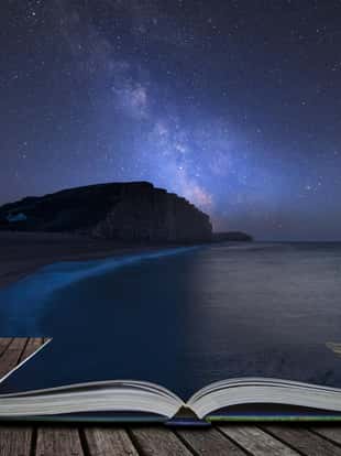 Stunning vibrant Milky Way composite image over landscape of long exposure of West Bay in Dorset coming out of pages in magical story book