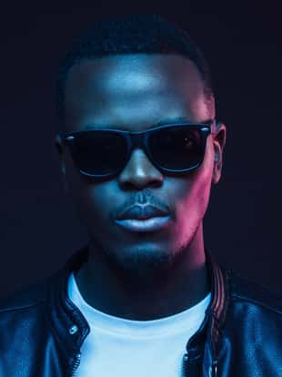 African male in sunglasses standing on night street in neon light