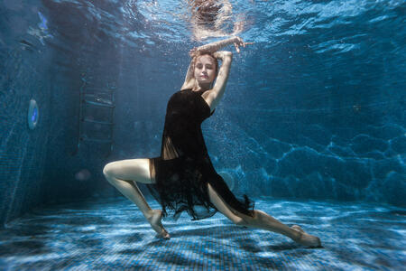 At the bottom of the pool, a woman in a dress is dancing under the water. Surrealistic photography.