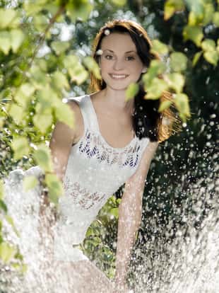 cute brunette in white dress standing behind water splash