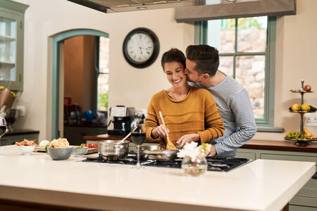 Shot of an affectionate young man kissing his wife on the cheek while she prepares a meal in the kitchen at home
