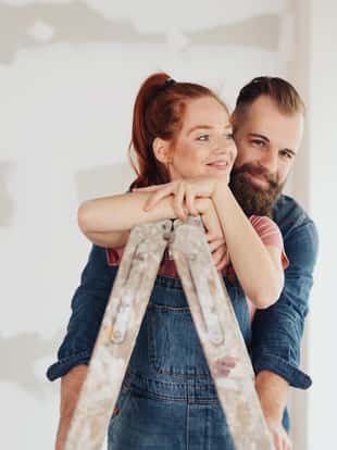 Loving young couple doing DIY home improvements renovating their house standing in an affectionate embrace with the woman leaning on a ladder on site