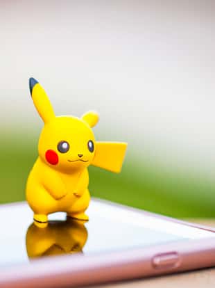 Peyton, Colorado, USA - August 17, 2016: A horizontal shot of the Pokemon Go character Pikachu, standing on top of an Apple iPhone 6 Plus. The character and phone are on a wall outdoors, in front of a defocused grassy area in Peyton, Colorado. The figurine is made by Tomy.