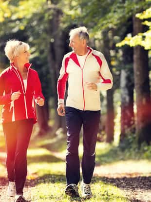 Senior Couple doing sport outdoors, jogging on a forest road in the autumn