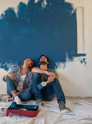 Thoughtful couple painting their house and looking up to the wall â redecorating concepts